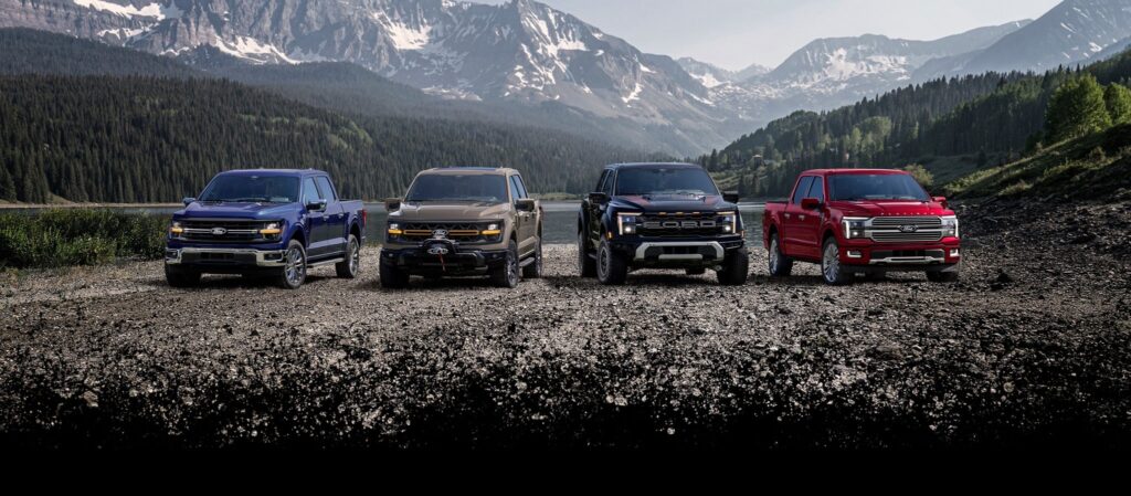 2026 Ford F-150 four trucks parked on gravel shore below mountains